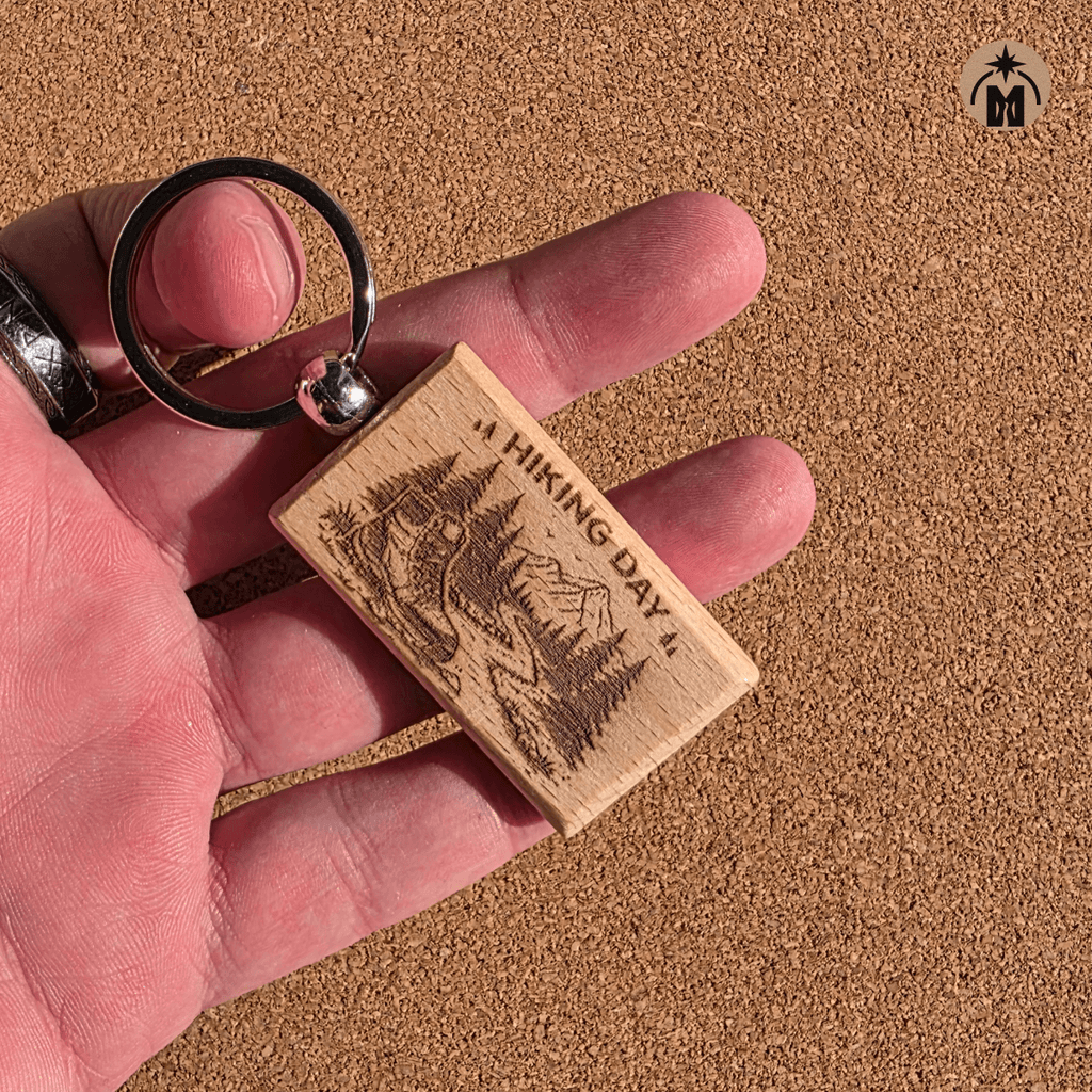 Beech wood keychain with hiking landscape engraving placed on rocky outdoor ground