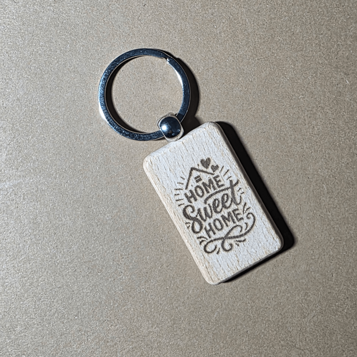 Engraved wooden keychain with “Home Sweet Home” text on beige background