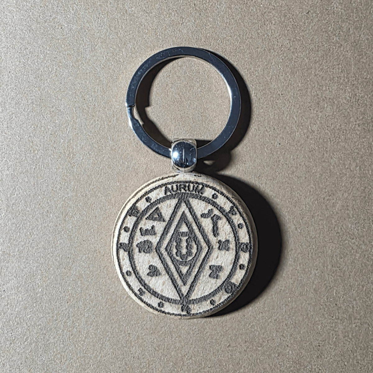 Light-finish wooden keychain with money-luck talisman motif (front)