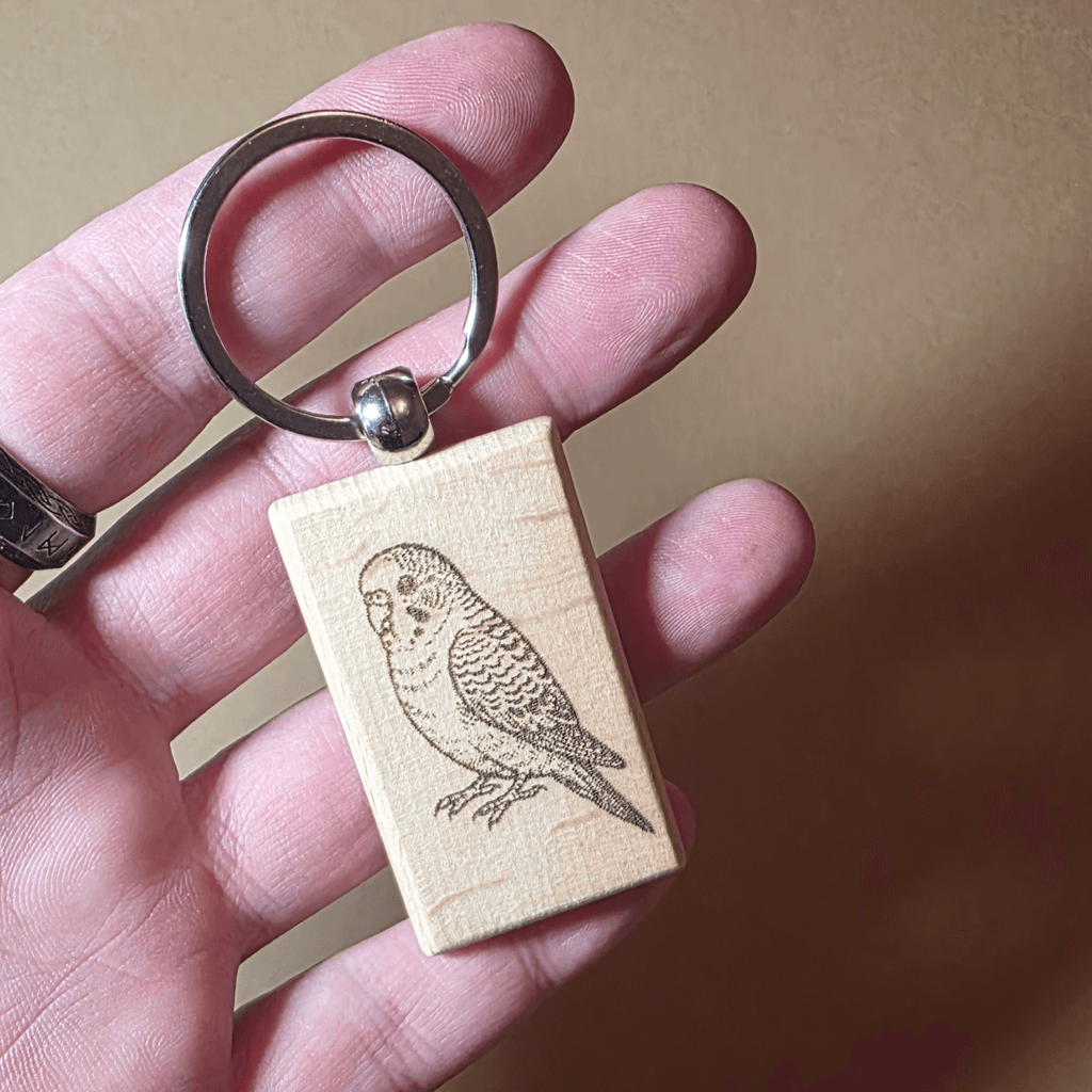 Natural wood budgie keychain on neutral background, gift for bird lovers