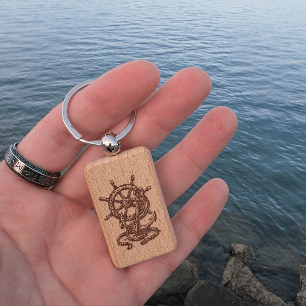 Engraved beech keychain with ship wheel motif held in hand over water