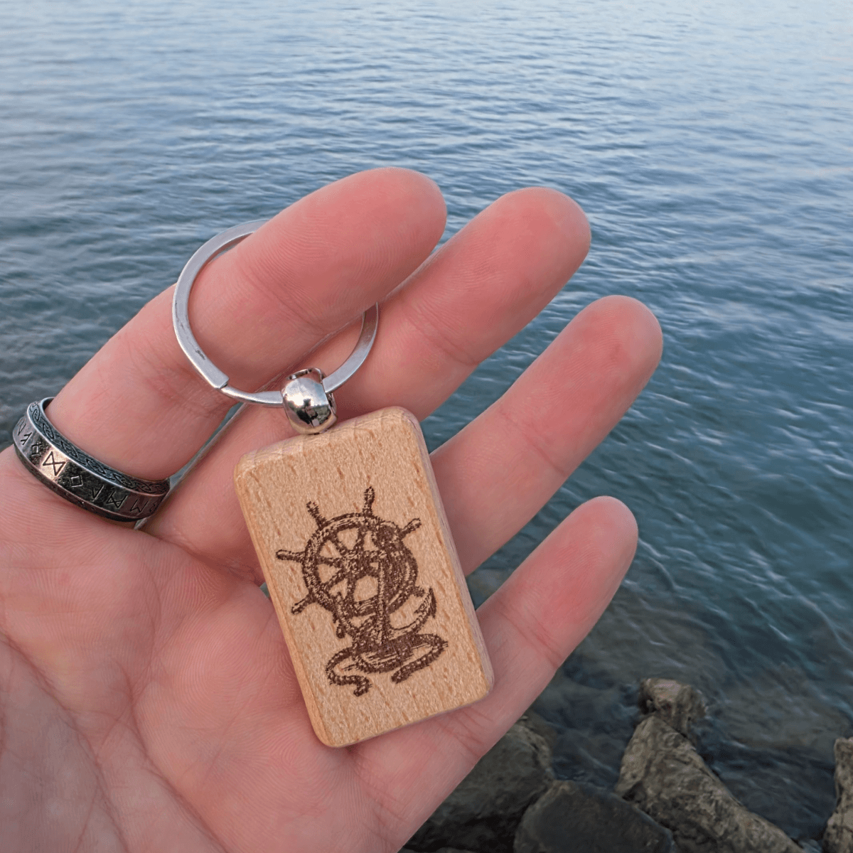 Engraved beech keychain with ship wheel motif held in hand over water