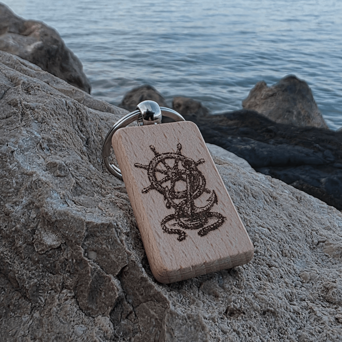 Nautical helm and anchor engraved wooden keychain on rock by the sea