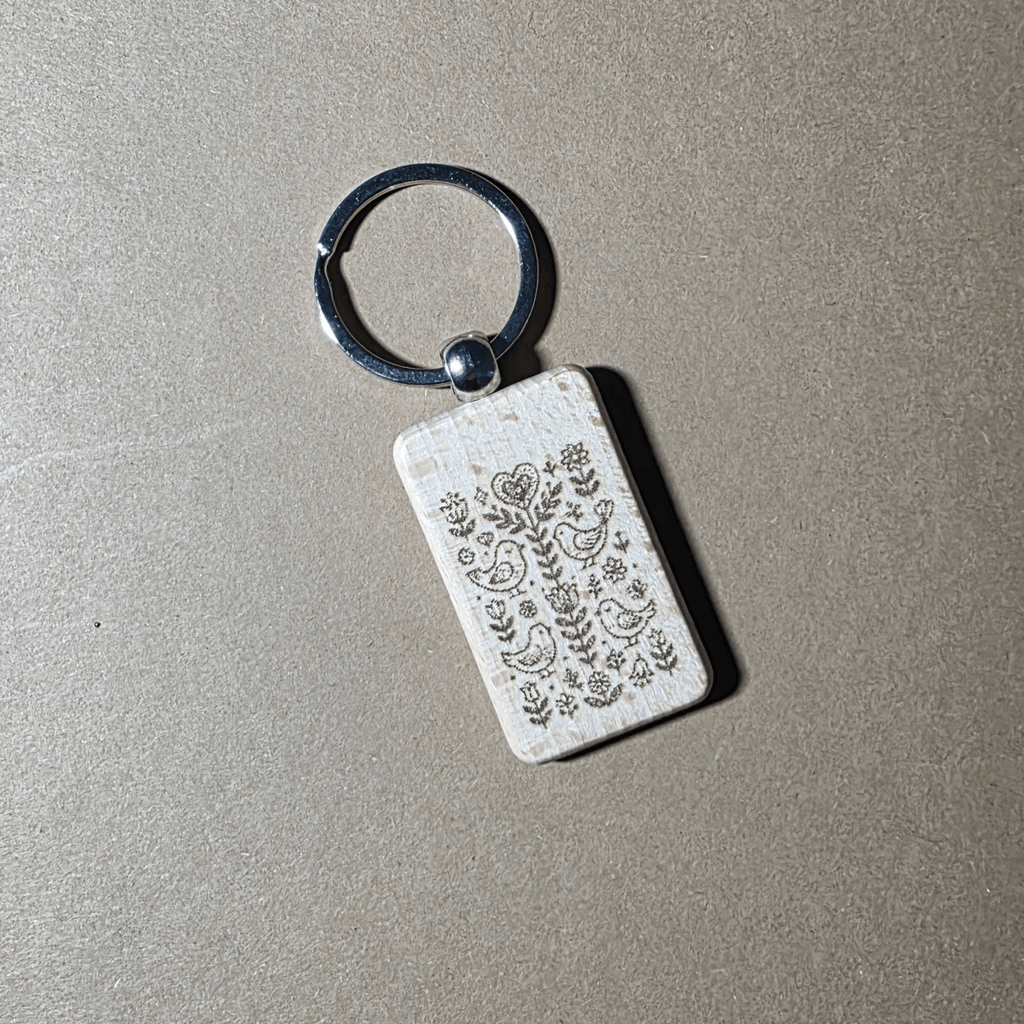 Scandi folk birds and flowers engraved wooden keychain on neutral background