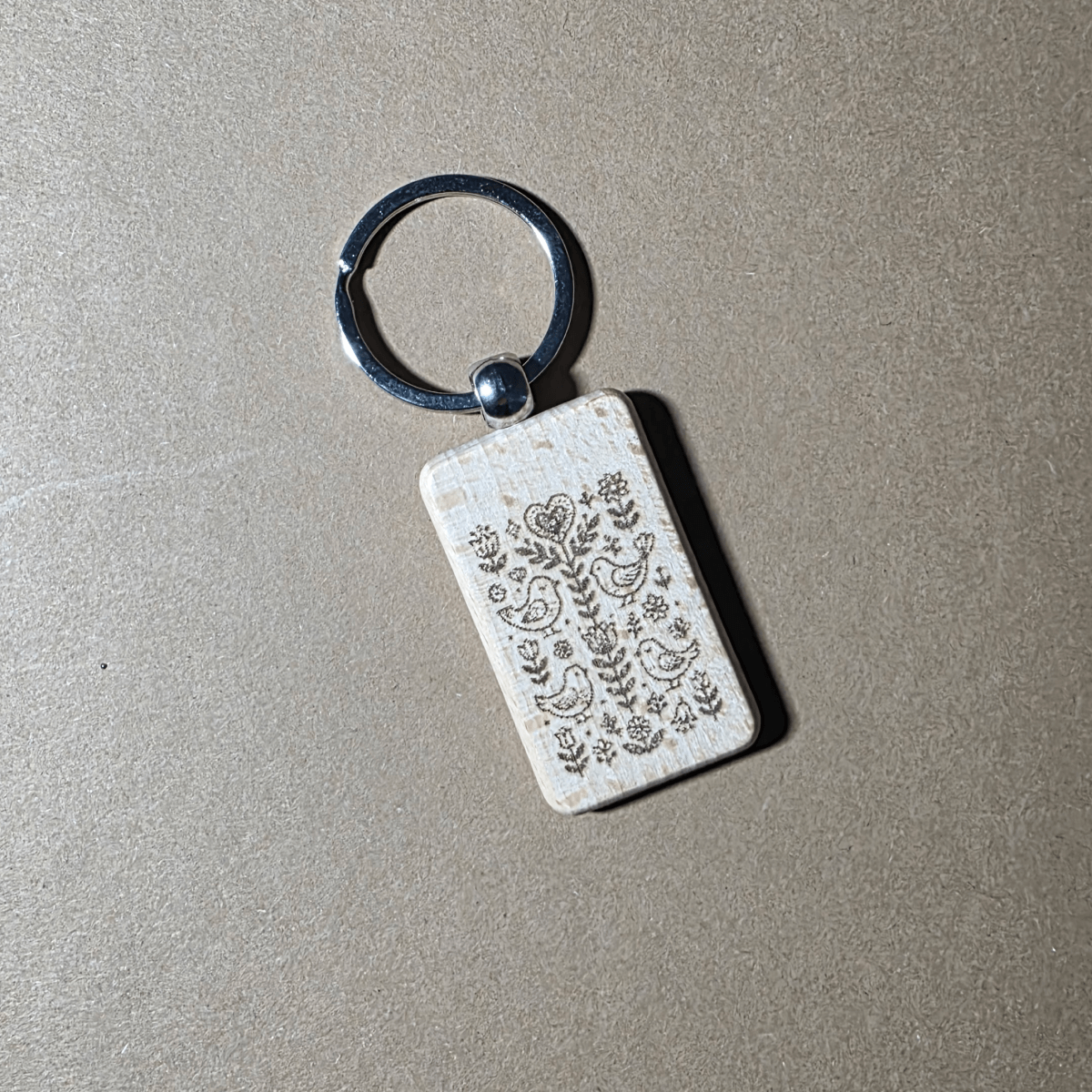 Scandi folk birds and flowers engraved wooden keychain on neutral background