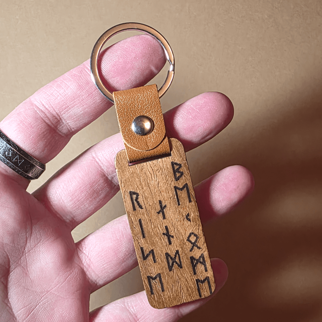 Engraved wooden Viking keychain in a hand showing the warrior and rune design with leather strap