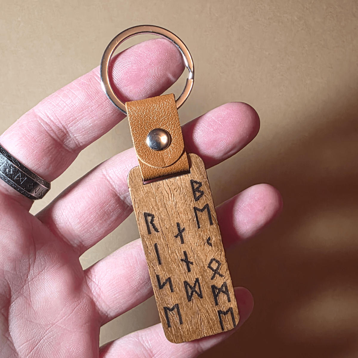 Engraved wooden Viking keychain in a hand showing the warrior and rune design with leather strap